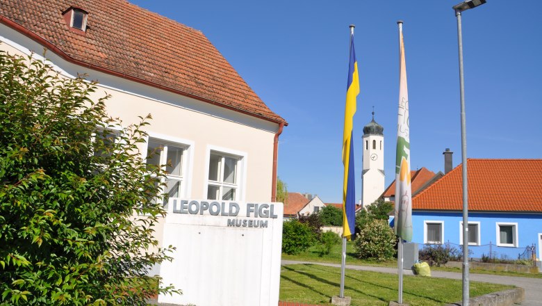 Leopold Figl Museum, © Stadtgemeinde Michelhausen Leopold Figl Museum mit Fahnen und Kirchturm im Hintergrund.