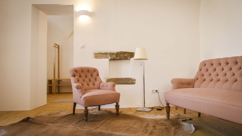 Oberstockstall Estate, © Robert Herbst Útulný obývací pokoj s křeslem, pohovkou, stojací lampou a kobercem na dřevěné podlaze.