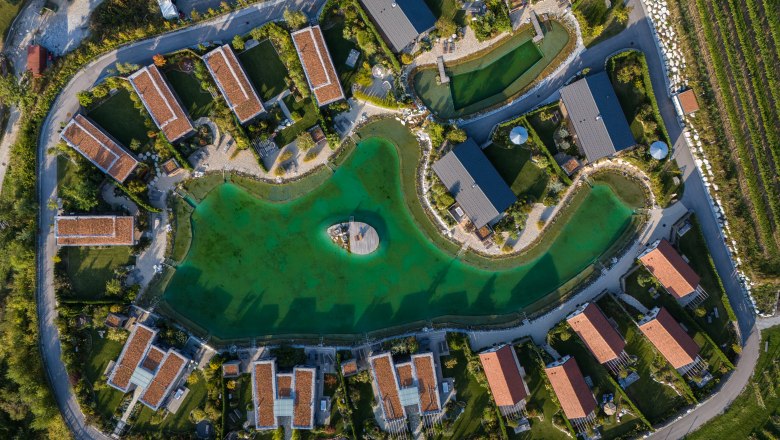 Chaty Kittenberger v Gartensee, © Niederösterreich Werbung / Maximilian Pawlikowsky Letecký pohled na chaty kolem zeleného jezera s molem uprostřed.