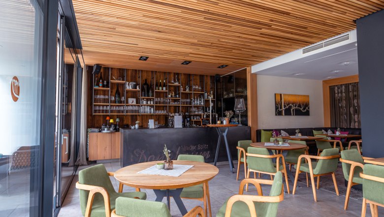 Boutique hotel WeinSpitz, © Niederösterreich Werbung / Maximilian Pawlikowsky Pohled do interiéru vinárny s dřevěnými prvky, zelenými židlemi a barem v pozadí.