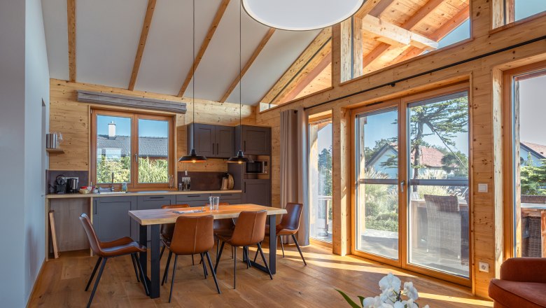 Chaty Kittenberger v Gartensee, © Niederösterreich Werbung / Maximilian Pawlikowsky Pohled do interiéru moderní chaty s dřevěnými trámy, jídelním stolem a velkými okny.