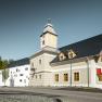 Hotel zum Glockenturm, © croce&wir Moderní budova se zvonicí a dřevěným obložením, obklopená stromy a jasnou oblohou.