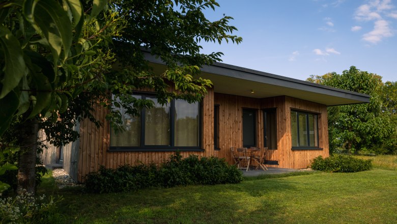 Chaty Grafenegg, © Niederösterreich Werbung / Maximilian Pawlikowsky Moderní dřevěný dům s velkými okny, obklopený stromy a trávníkem.