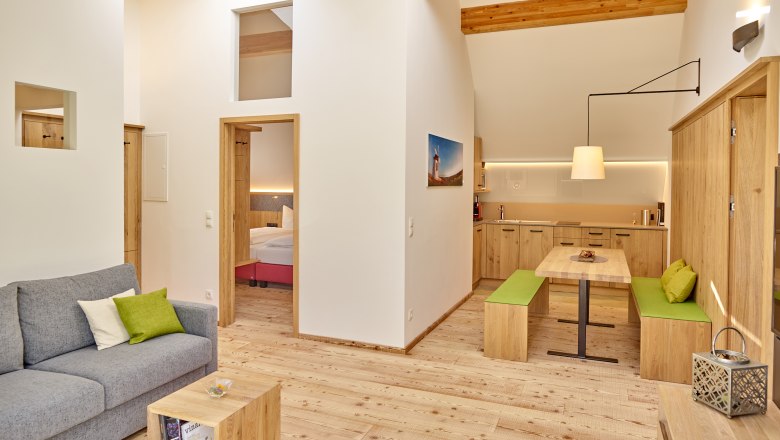 Weinviertler Kellerstöckl, © Weingut Hindler Moderní obývací pokoj s dřevěným nábytkem, šedou pohovkou a otevřenou kuchyní.