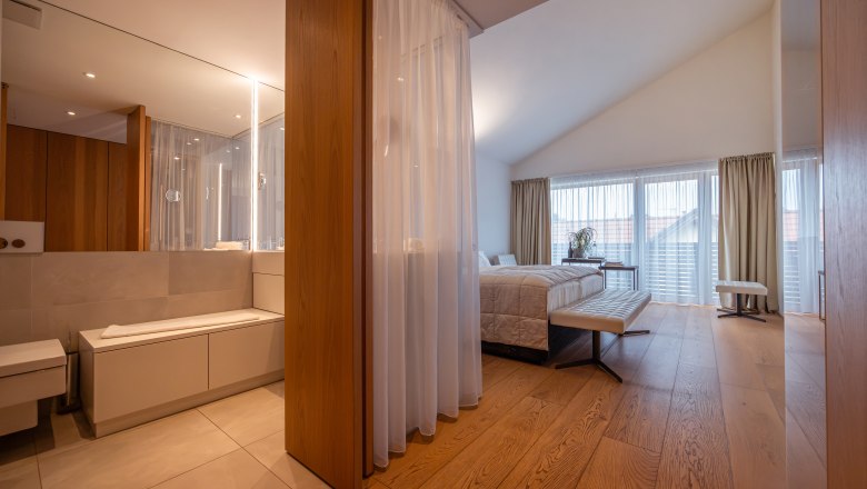 Relais & Chateaux MÖRWALD Hotel am Wagram, © Niederösterreich Werbung / Maximilian Pawlikowsky Moderní hotelový pokoj s dřevěnou podlahou, velkou postelí a koupelnou se zrcadlem.