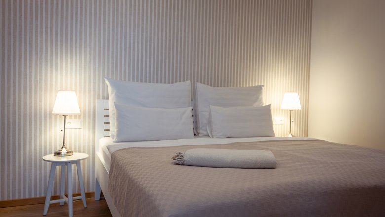 Apartmány Hausgnost, © Niederösterreich Werbung / Maximilian Pawlikowsky Moderní ložnice s manželskou postelí, nočními stolky a lampičkami.