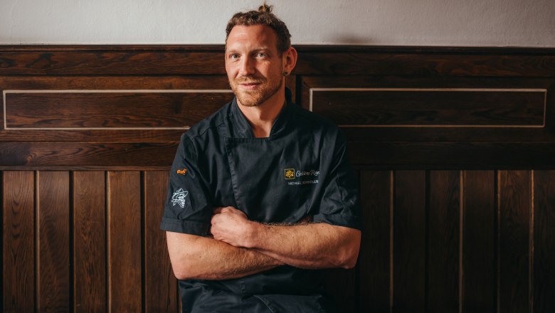 Pronajímatel Michael Schindler, © Niederösterreich Werbung/Daniela Führer Před dřevěnou stěnou sedí muž v černé kuchařské bundě.