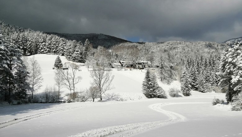 Venkovské sídlo Oberhof v zimě, © Landsitz Oberhof Zasněžená krajina s lesy a kopci, tmavé mraky na obloze.