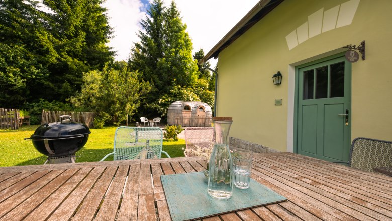 Dovolená v BAHNhofu, © Niederösterreich Werbung / Maximilian Pawlikowsky Zahrada s dřevěným stolem, židlemi, grilem a saunou ve tvaru sudu.