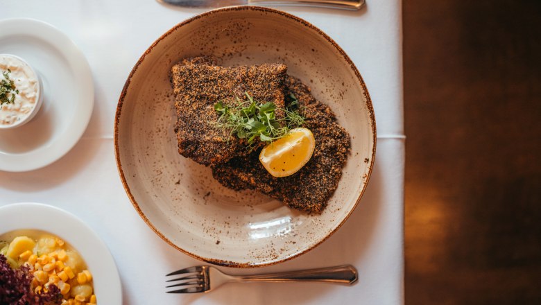 Filet z kapra Waldviertel z opatství Zwettl obalený v šedém máku, © Niederösterreich Werbung/Daniela Führer Kapří filet obalený v šedé makové polevě s plátkem citronu a bylinkami na talíři, s přílohou.