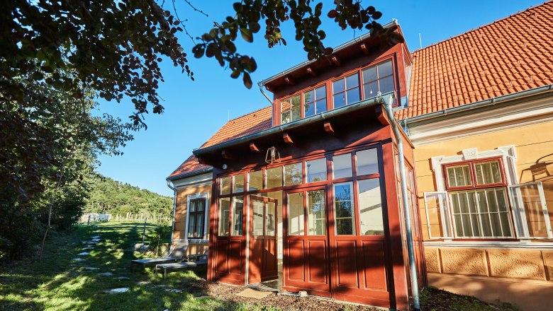 Villa Tranquillini, © Herbert Lehmann Žlutá vila s červenými střešními taškami a proskleným vchodem, obklopená stromy a zelenou zahradou.