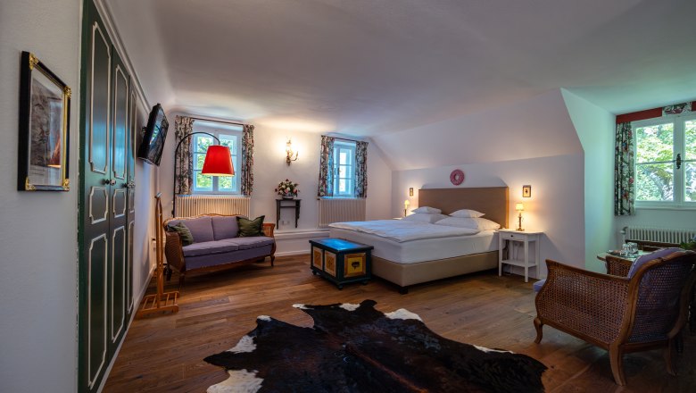 Venkovské sídlo Oberhof, © Niederösterreich Werbung / Maximilian Pawlikowsky Útulná ložnice s manželskou postelí, pohovkou, dřevěnou podlahou a kobercem z hovězí kůže.