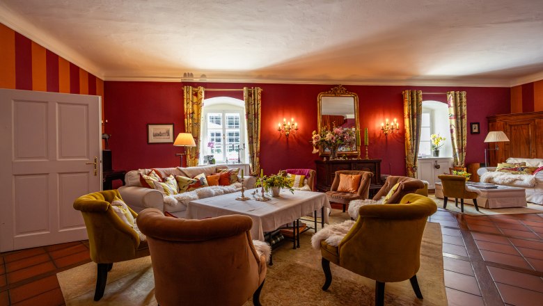 Lesnická chata Langschlägerwald, © Niederösterreich Werbung / Maximilian Pawlikowsky Elegantní obývací pokoj s červenými stěnami, pohodlnými křesly a velkým zrcadlem.