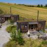 SONNENTOR country lofts, © Niederösterreich Werbung / Maximilian Pawlikowsky Dva rustikální dřevěné domy se zelenými střechami ve venkovském prostředí.