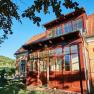 Villa Tranquillini, © Herbert Lehmann Žlutá vila s červenými střešními taškami a proskleným vchodem, obklopená stromy a zelenou zahradou.