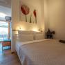 Apartmány Hausgnost, © Niederösterreich Werbung / Maximilian Pawlikowsky Moderní ložnice s manželskou postelí, světlou dřevěnou podlahou a uměleckými díly na stěnách. Dveře vedou na balkon s výhledem na střechy.