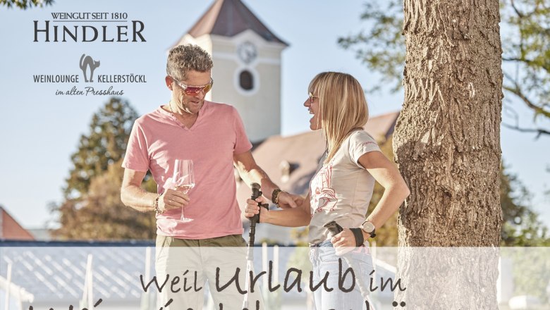 Vinařství Hindler, © Weingut Hindler Muž a žena stojí před stromem se sklenicemi na víno a vycházkovými holemi, v pozadí budova s věží.