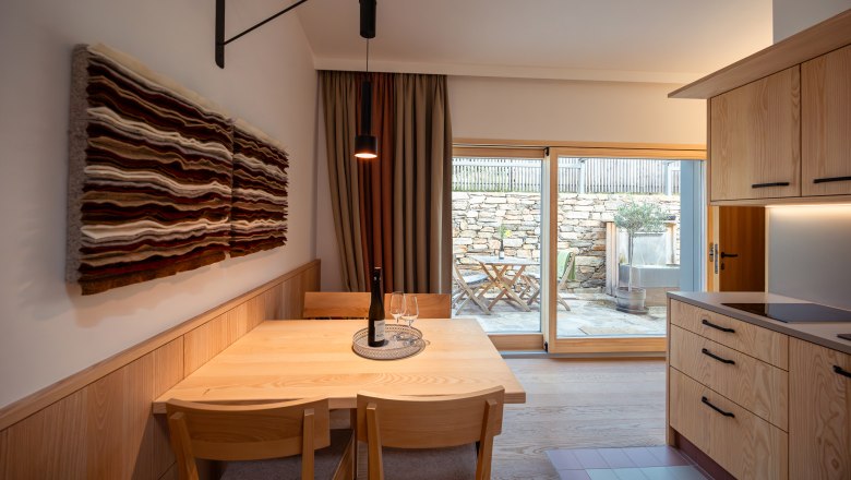 Weinviertler Kellerstöckl Vinařství Hindler, © Niederösterreich Werbung / Maximilian Pawlikowsky Pohled do interiéru moderní jídelny s dřevěným nábytkem a uměleckými díly na stěnách, pohled na terasu přes skleněné dveře.