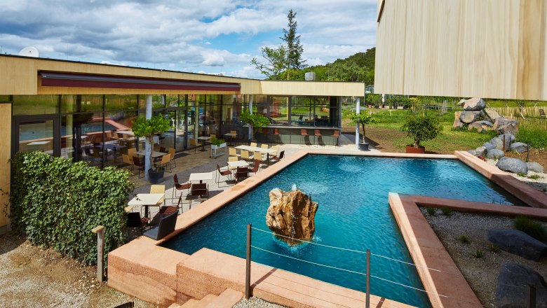 Veranda: Snídaně a svačina u leknínového jezírka, © Gut Guntrams- Picasa Moderní terasa se stoly a židlemi u obdélníkového jezírka s kameny uprostřed.