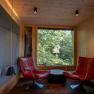 Treehouse Lodge Schrems, © Niederösterreich Werbung / Maximilian Pawlikowsky Pohled do interiéru moderního domku na stromě se dvěma červenými křesly před velkým oknem s výhledem na les.