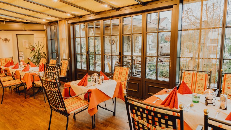 Zimní zahrada a zahrada pro hosty, © Niederösterreich Werbung/Klaus Engelmayer Útulná zimní zahrada se stoly a židlemi, obklopená velkými okny s výhledem ven.