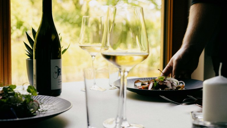 Restaurace ve vinařství Johnneshof Reinisch, © Julius Hirtzberger Prostřený stůl s lahví vína, sklenicemi a talířem s jídlem v restauraci.