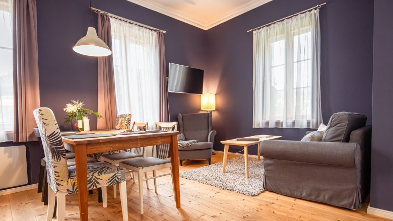 Dovolená v hotelu BAHNhof, © Niederösterreich Werbung / Maximilian Pawlikowsky Útulný obývací pokoj s dřevěnou podlahou, jídelním stolem, židlemi, křeslem a pohovkou.