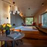 Treehouse Lodge Schrems, © Niederösterreich Werbung / Maximilian Pawlikowsky Pohled do interiéru moderního domku na stromě s dřevěnými stěnami, postelí, stolem s květinami a velkými okny s výhledem do zeleně.