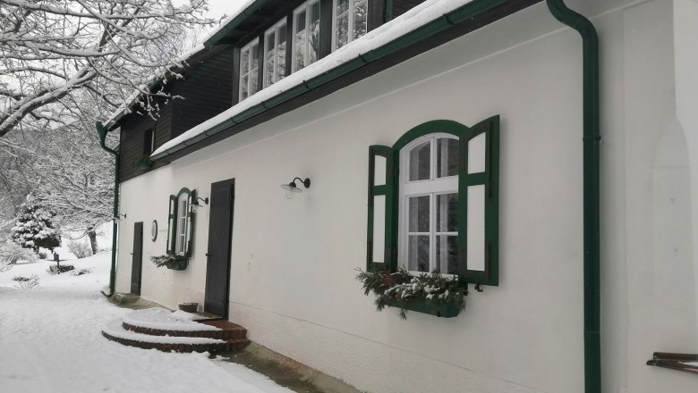 Venkovské sídlo Oberhof, © Landsitz Oberhof Zasněžený dům se zelenými okenicemi a okapy.