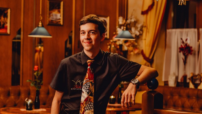 Dominik Semper, © Niederösterreich Werbung/Klaus Engelmayer Mladý muž v restauraci s kravatou a košilí, usmívá se.