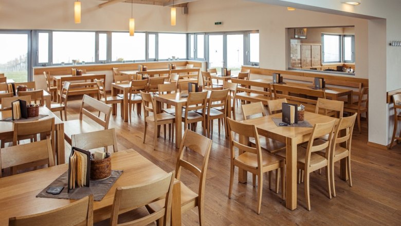 Pohled do interi&eacute;ru elegantn&iacute;ho heurigera s dřevěn&yacute;m n&aacute;bytkem a velk&yacute;mi okny.