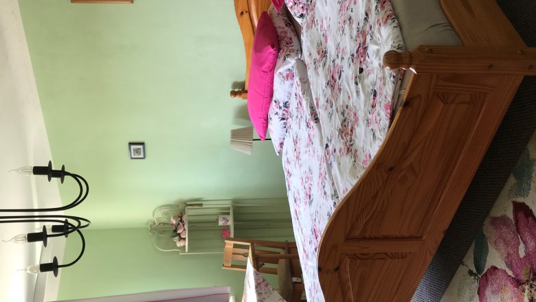 Ložnice s manželskou postel&iacute;, zelen&yacute;mi stěnami, květinov&yacute;m ložn&iacute;m pr&aacute;dlem, stolem se židlemi, z&aacute;věsy a lustrem.