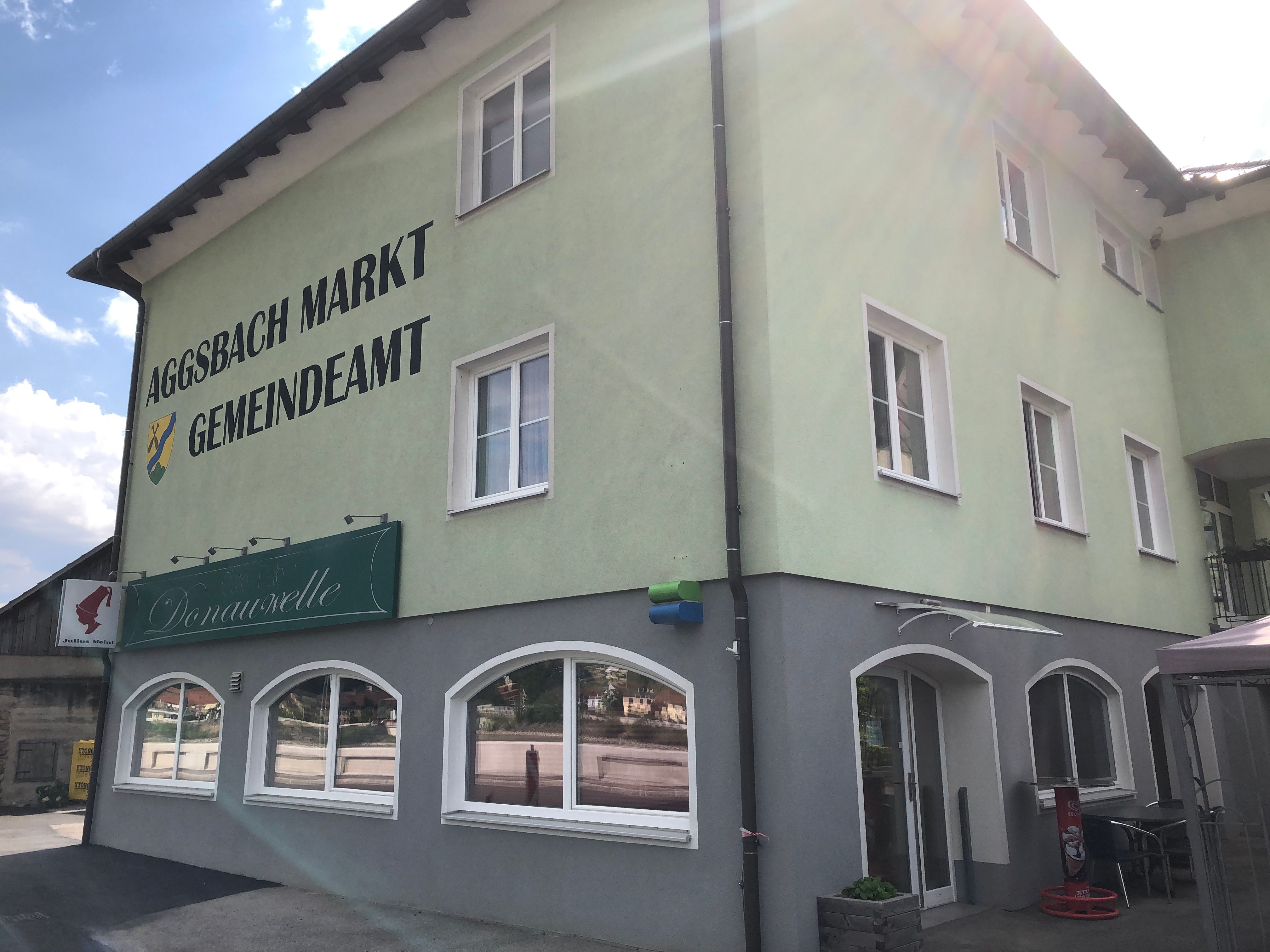 Zelená budova s označením "Aggsbach Markt Gemeindeamt" a kavárna Donauwelle.