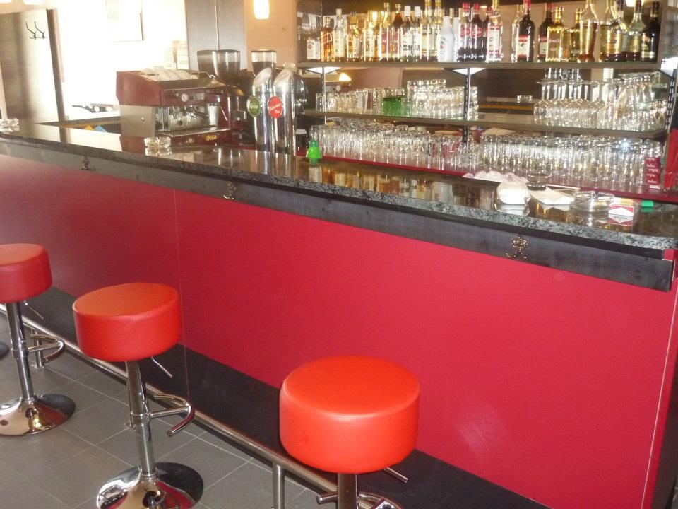 Pohled do interiéru baru s červenými stoličkami a dobře zásobeným pultem.