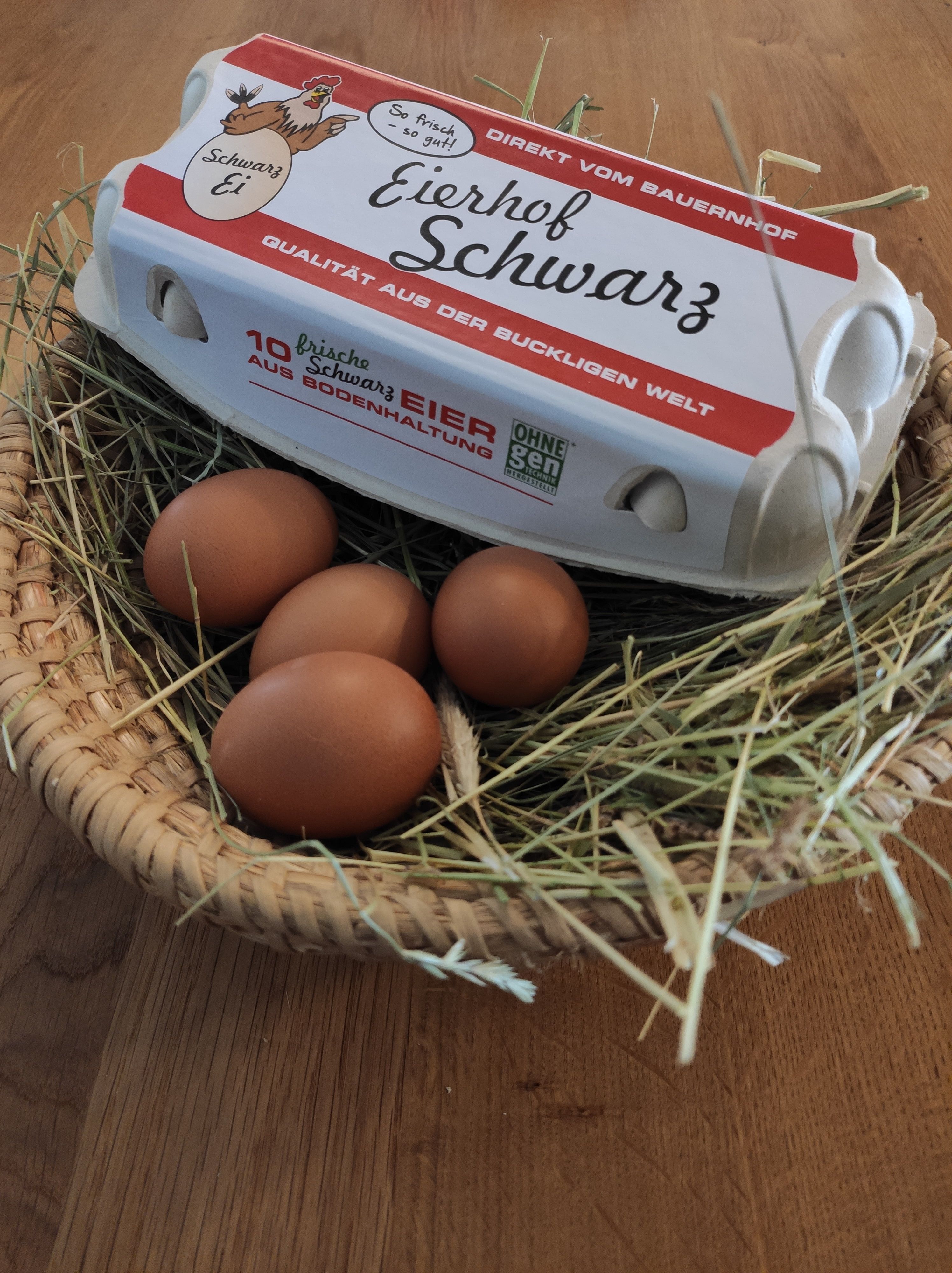 Na košíku se slámou a hnědými vejci leží karton na vejce s nápisem "Eierhof Schwarz".