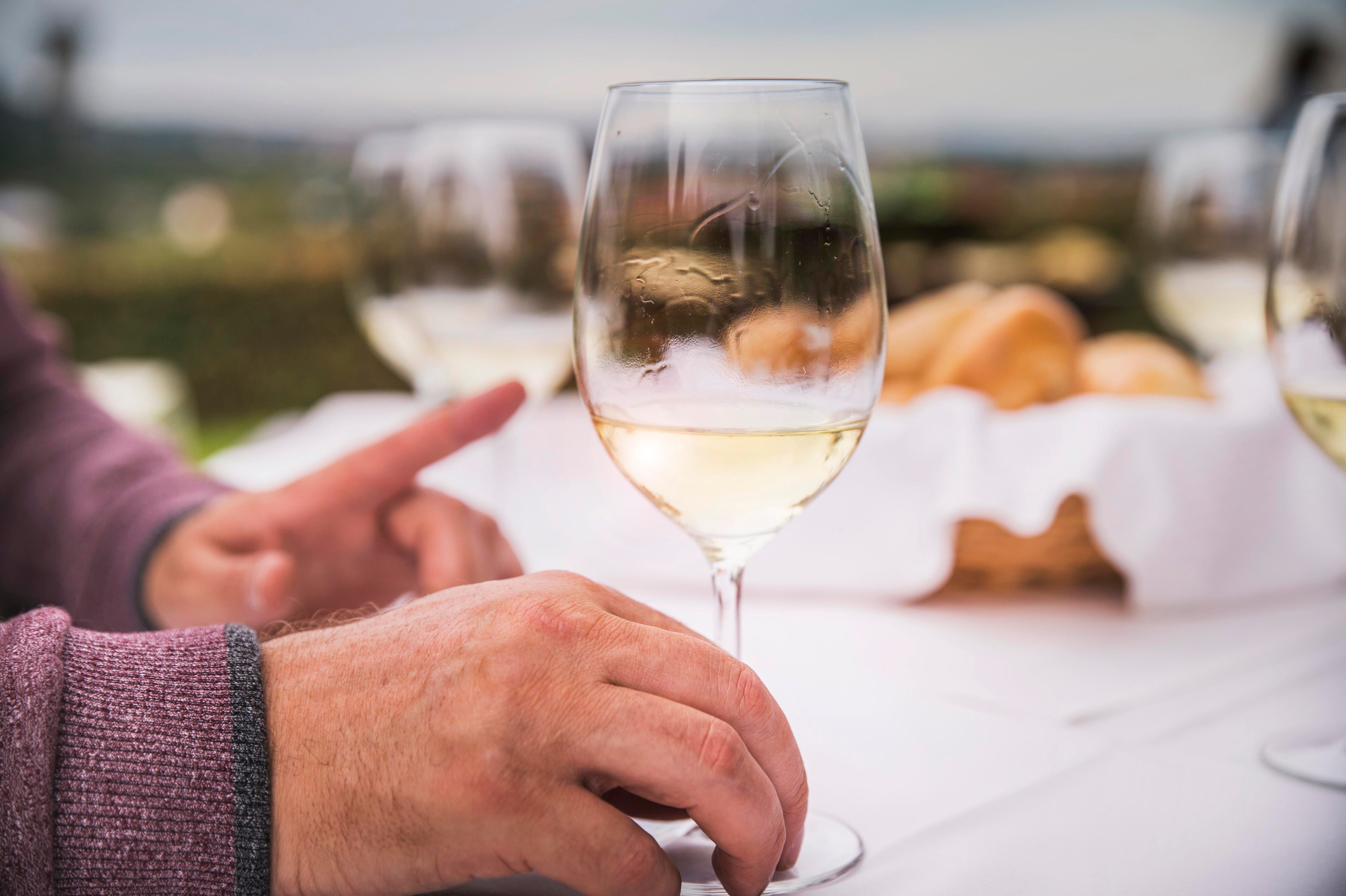 Detailní záběr rukou se sklenicí na víno na položeném stole venku.