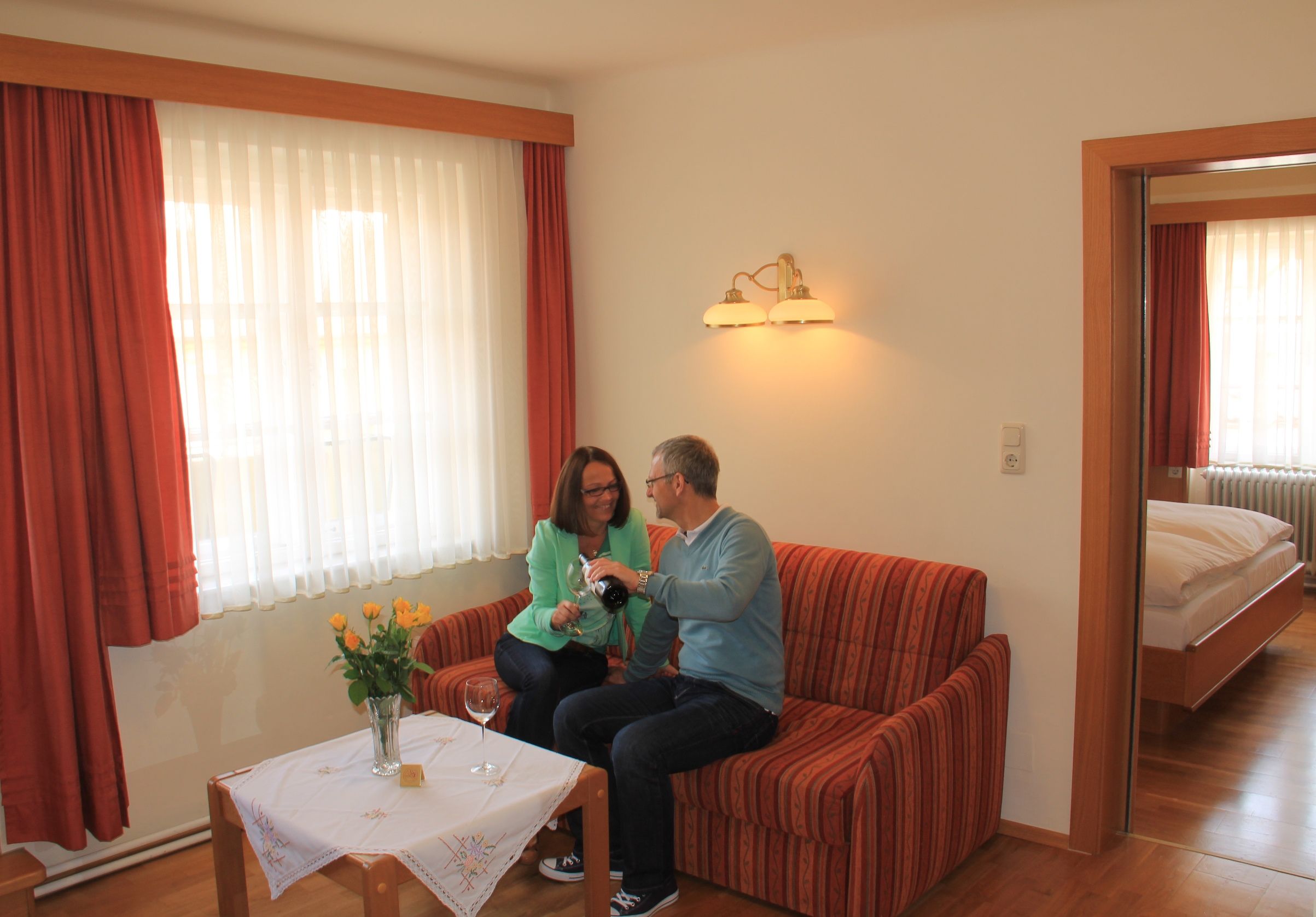 Pár sedí na pohovce v útulném bytě a nalévá si víno.