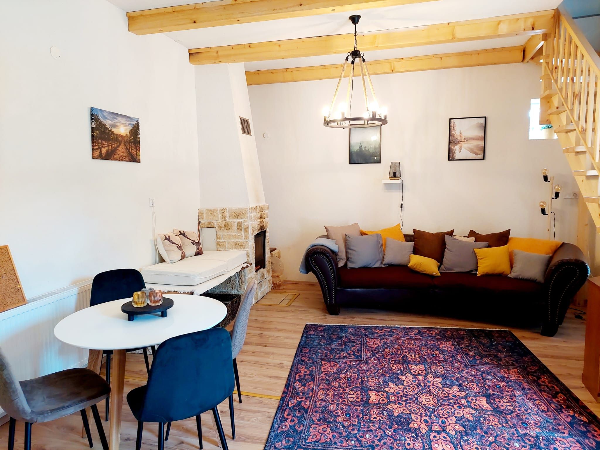 Útulný obývací pokoj/jídelna s dřevěnými trámy, pohovkou, jídelním stolem a krbem.