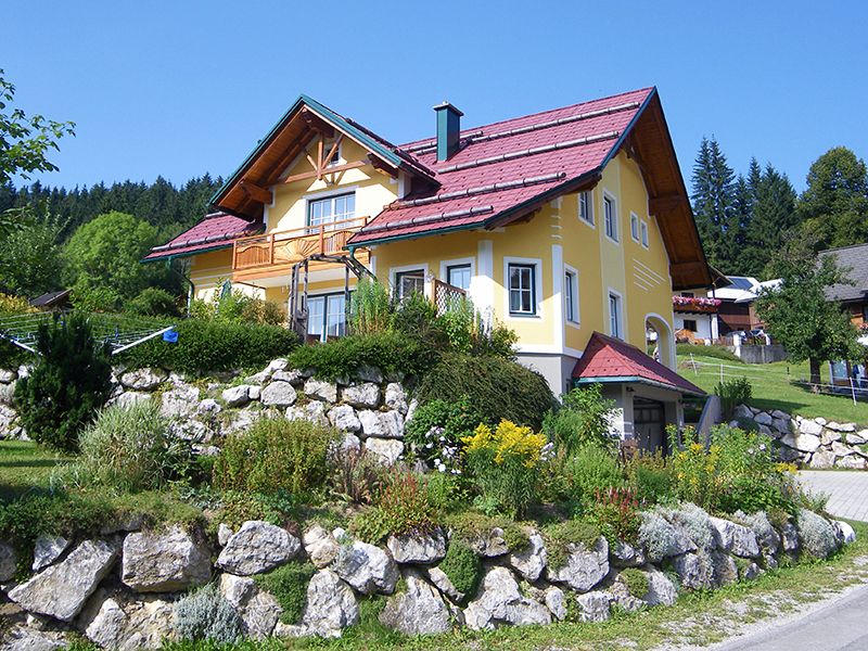 Žlutý dům s červenou střechou v zelené krajině.