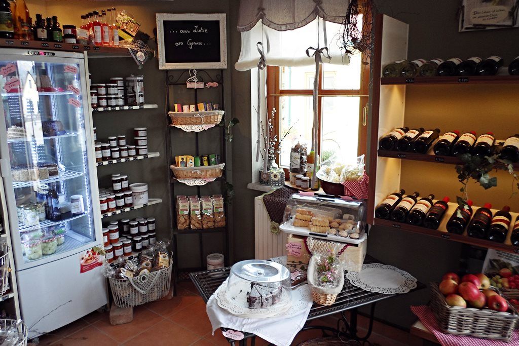 Pohled do interiéru farmářského obchodu s regály plnými lahví vína, džemů a pečiva.