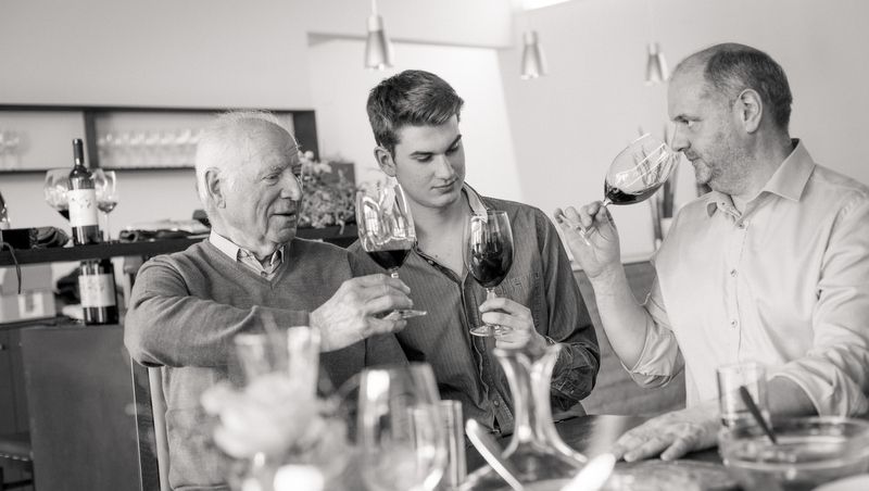 Tři muži si u stolu cinknou skleničkami vína.