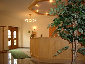 Recepce hostince s dřevěným pultem a rostlinami.