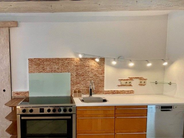 Moderní kuchyňská linka se sporákem, dřezem a myčkou nádobí před mozaikovou obkladovou stěnou.