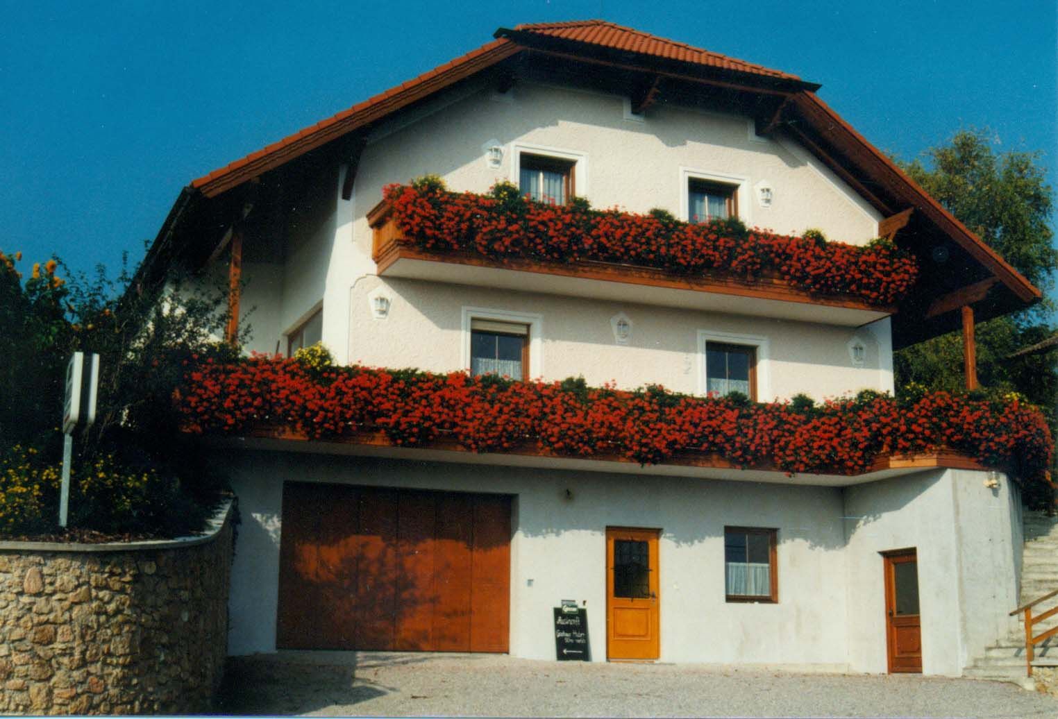 Tradiční penzion s červenými květinami na balkonech a červenou střechou.
