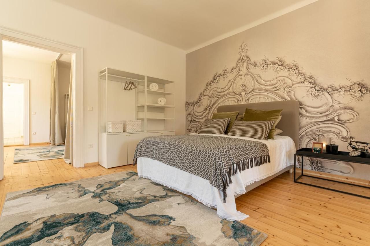 Stylově zařízená ložnice s velkou postelí, dekorativními polštáři, kobercem a uměleckým designem stěn.