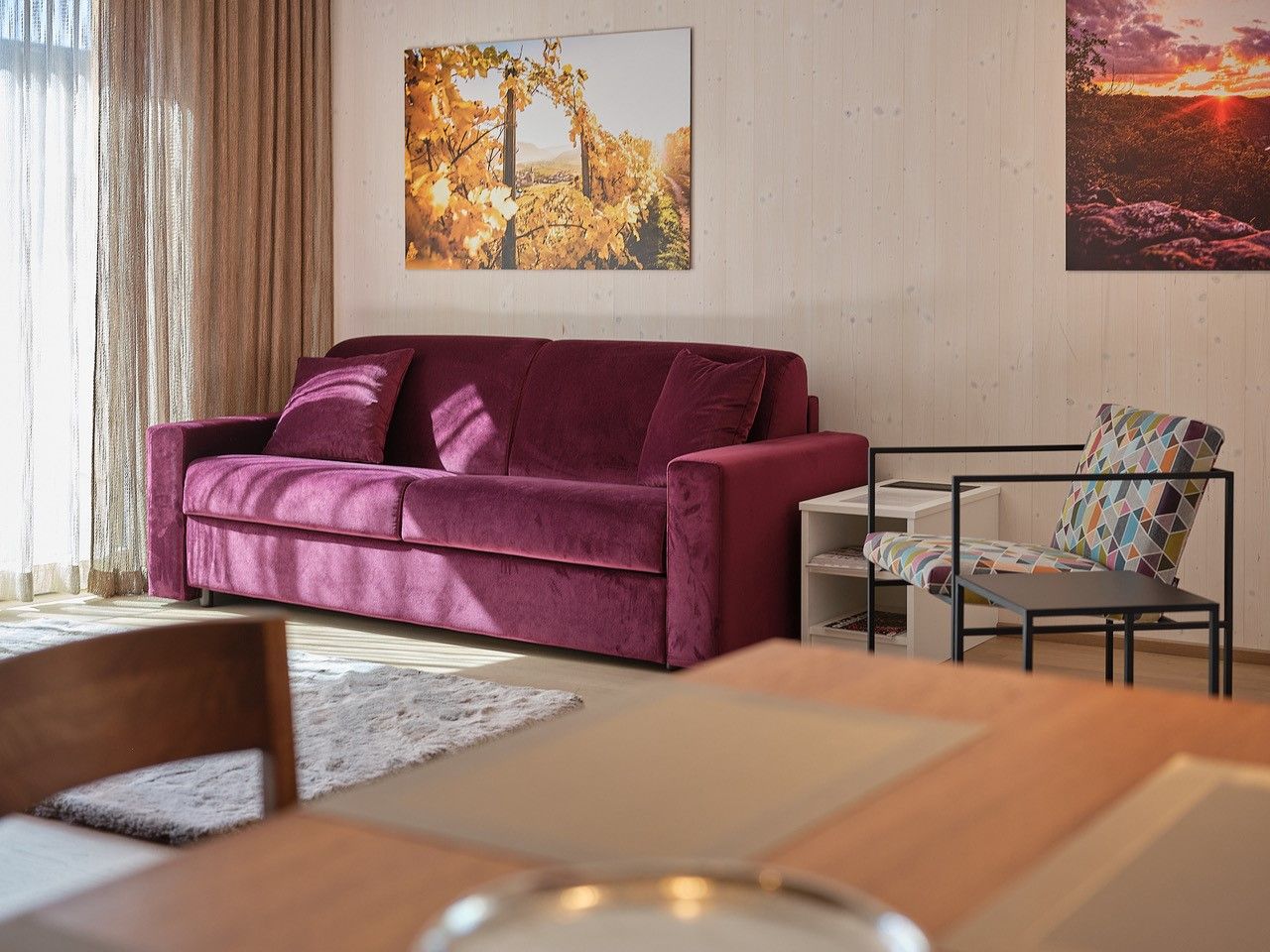 Obývací pokoj s fialovou pohovkou, barevným křeslem a nástěnnými malbami.