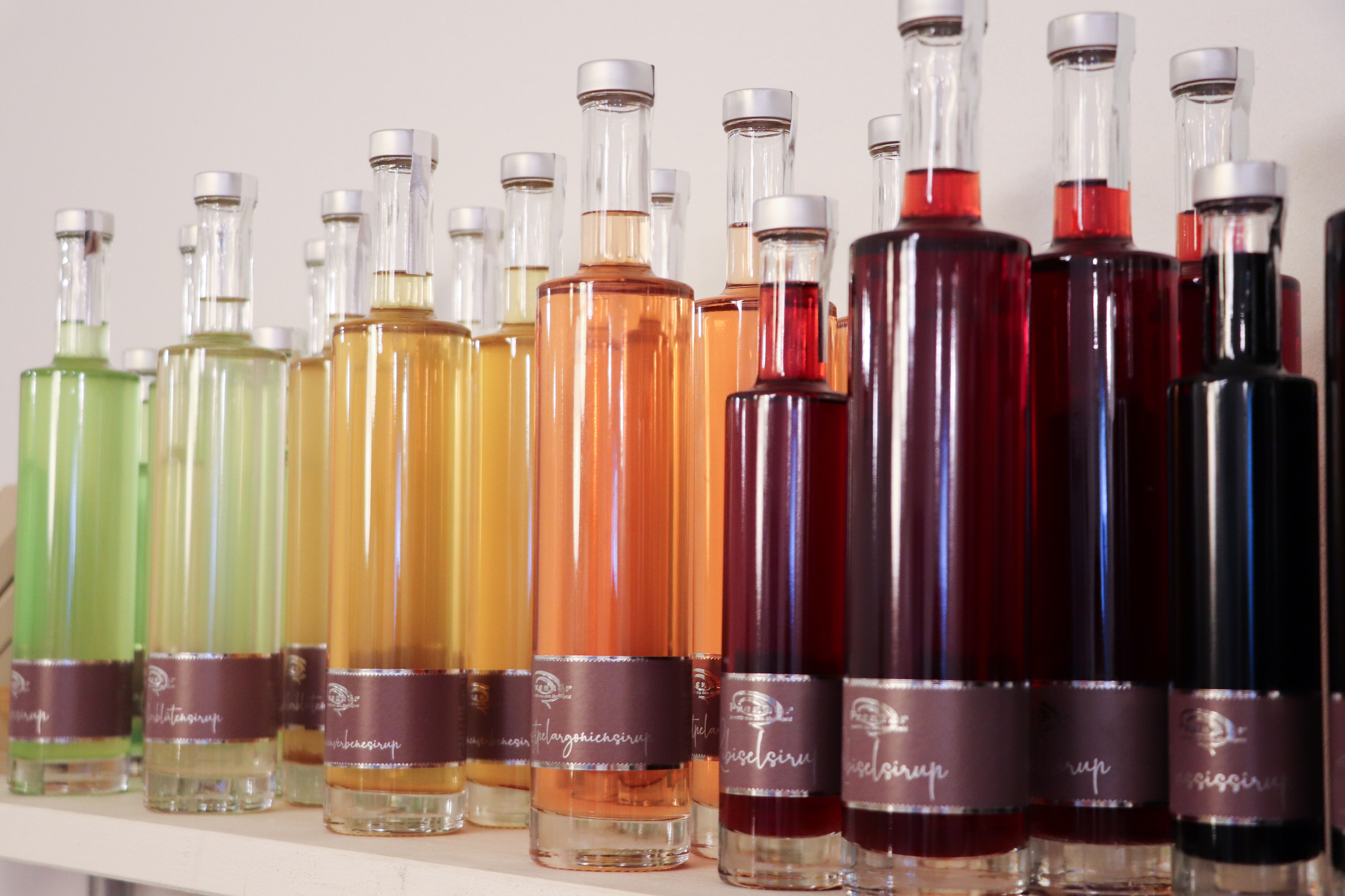 Různé barevné lahve se sirupem v řadě na polici.