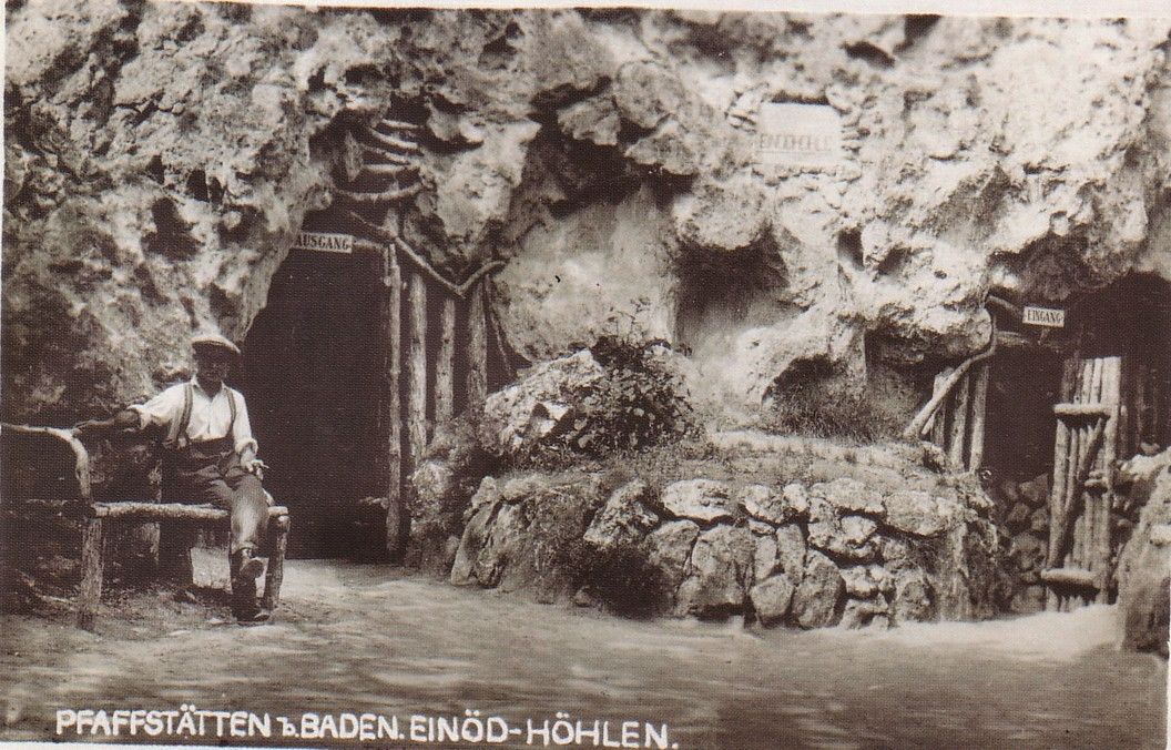 Historická fotografie jeskyně Einödhöhle v Pfaffstätten v Bádensku s mužem na lavičce před vchodem do jeskyně.