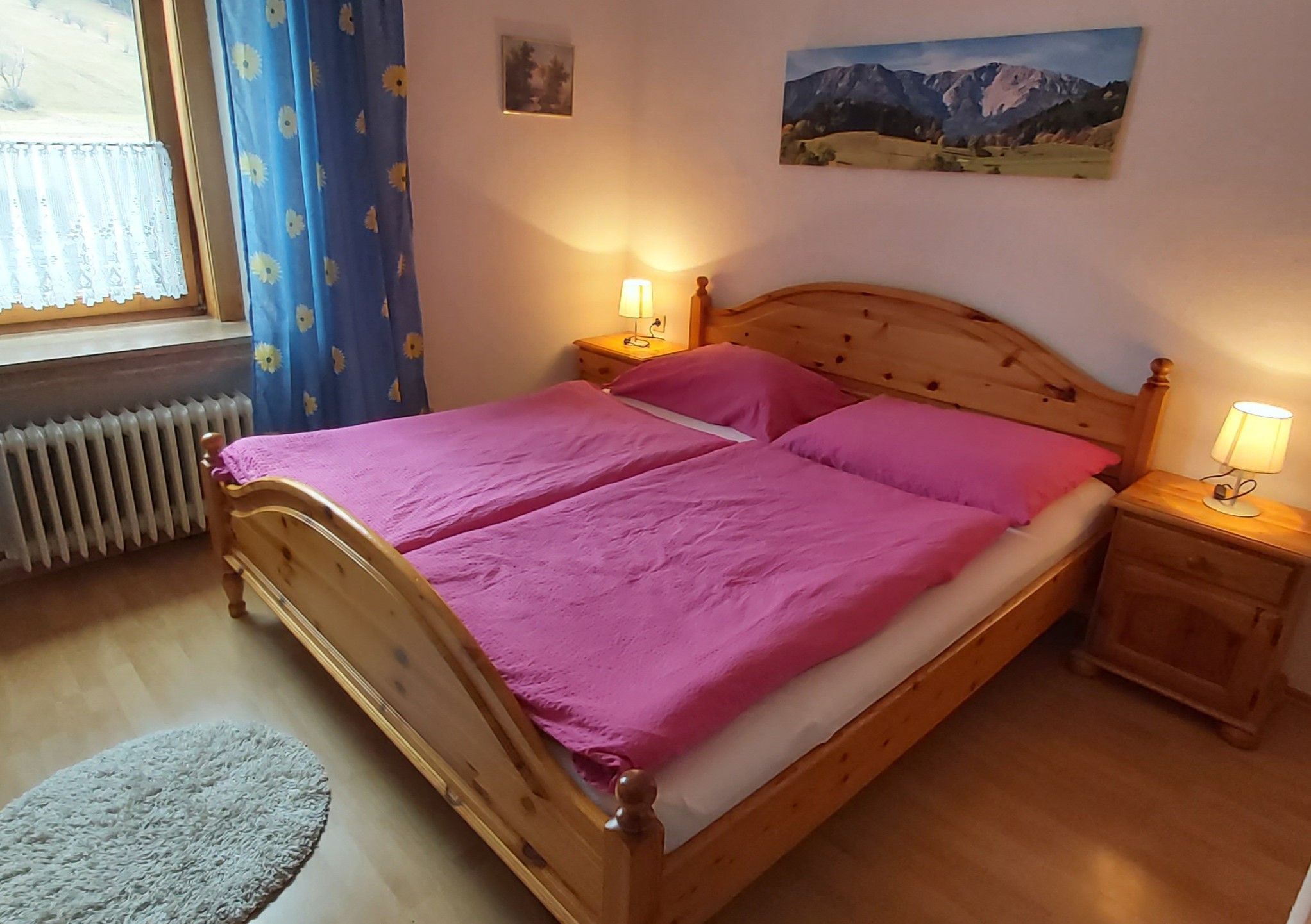 Útulný dvoulůžkový pokoj s dřevěnou postelí, růžovým ložním prádlem a nočními stolky s lampičkami.