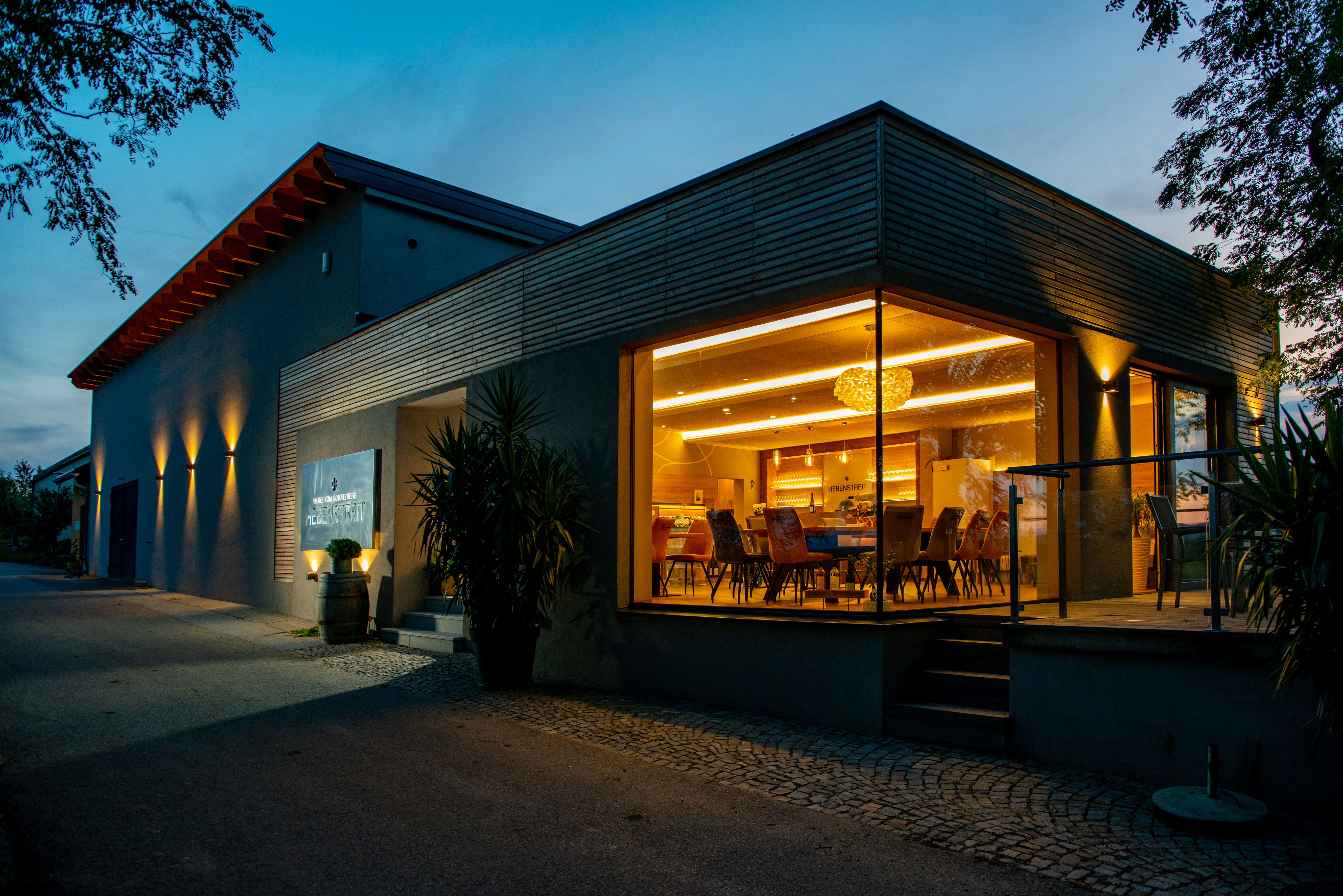 Moderní budova s proskleným průčelím a vnitřním osvětlením za soumraku.